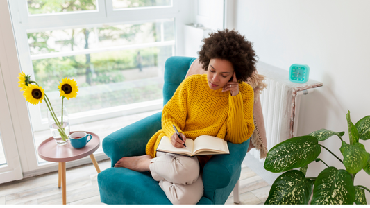 a woman sitting on a blue chair and writing on a diary