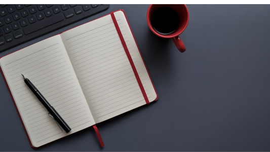 an open notebook with a pen, a cup of coffee, and a grey backdrop