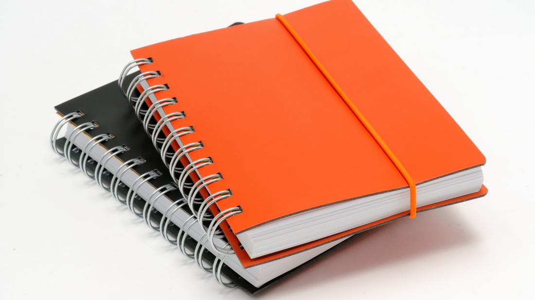 two notebooks on top of one another, one black and one orange