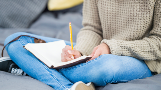 a person sitting on a bed writing on a notebook or diary